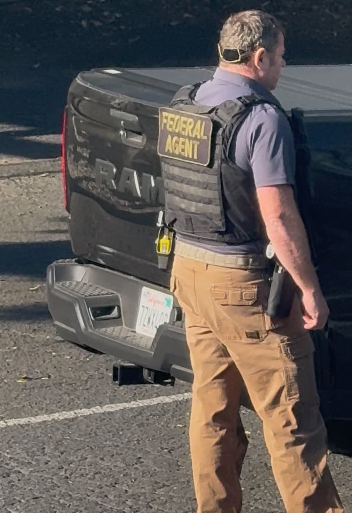 An agent in a vest placarded "FEDERAL AGENT" beside a black RAM pickup. None of the vehicles at the scene carried light bars, agency decals or government plates.